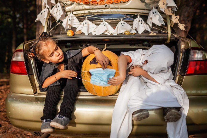 Kids Dressed in Halloween Costumes Sitting in Car Trunk Putting Mask on Pumpkin